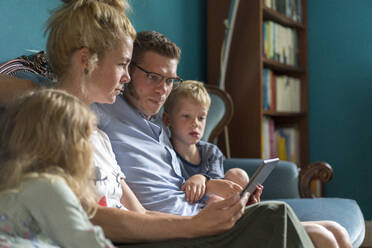 Family with digital tablet sitting on sofa in living room at home - MOEF03110