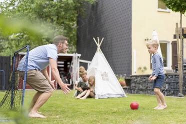 Mann und Sohn spielen Fußball, während die Frau mit ihrer Tochter im Zelt im Hinterhof sitzt - MOEF03113