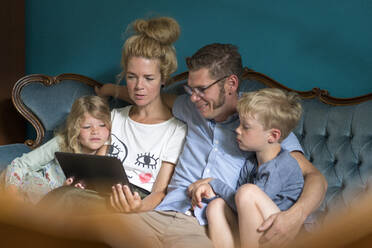 Woman sharing digital tablet with family while sitting on sofa in living room at home - MOEF03114