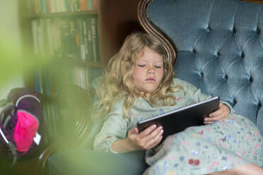 Blondes Mädchen entspannt auf Sofa mit digitalem Tablet im Wohnzimmer zu Hause - MOEF03130