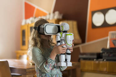 Mädchen mit Virtual-Reality-Simulator-Headset hält Roboter beim Spielen im Wohnzimmer zu Hause - MOEF03139