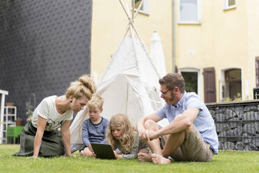 Family enjoying weekend at back yard with girl using digital tablet - MOEF03145
