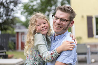 Smiling man carrying blond daughter at back yard - MOEF03161