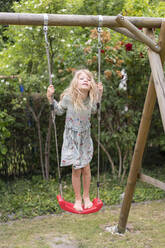 Blond girl standing on swing at back yard - MOEF03164