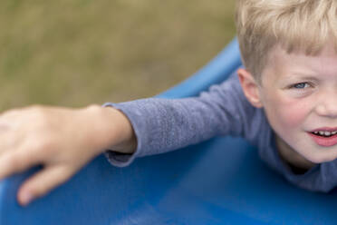 Blond boy lying on blue slide at back yard - MOEF03165