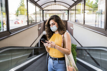 Junge Frau schreibt SMS, während sie mit einer Netztasche auf dem Laufsteg einer U-Bahn steht - EBBF00622