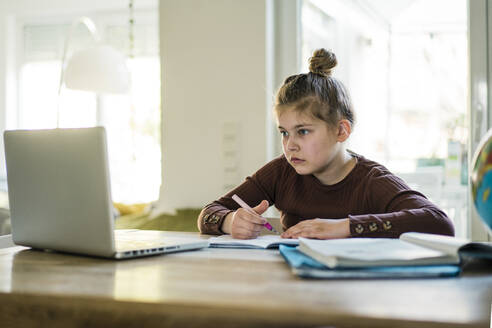 Girl writing in book while studying through laptop at home - JOSEF01480