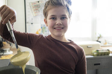 Lächelndes süßes Mädchen mit Schöpfkelle bei der Zubereitung von Waffelteig in der Küche - JOSEF01500
