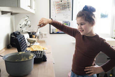 Cute girl with ladle preparing waffle in kitchen - JOSEF01502