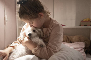 Cute girl embracing dog while sitting in bedroom - JOSEF01507