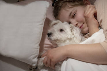 Cute girl holding dog while lying down in bedroom - JOSEF01512