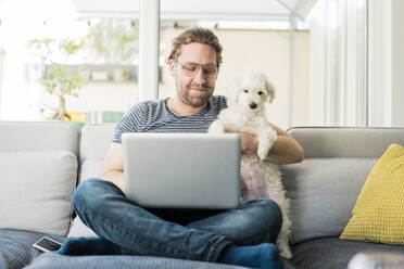 Mann mit Laptop und Hund auf dem Sofa sitzend - JOSEF01524