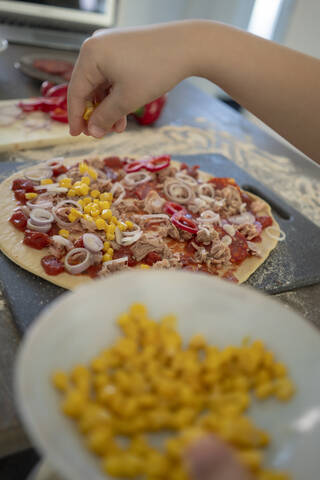 Ausgeschnittenes Bild eines Mädchens, das Mais einschenkt, während es in der Küche eine Pizza zubereitet, lizenzfreies Stockfoto