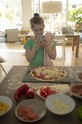 Girl photographing pizza over kitchen island stock photo