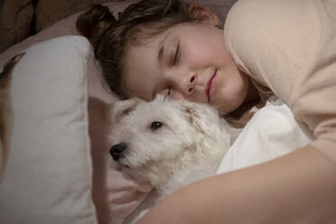Cute girl holding dog while sleeping in bedroom - JOSEF01552