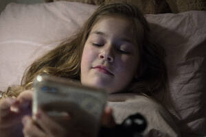 Mädchen, das im Schlafzimmer liegend ein Smartphone benutzt - JOSEF01553