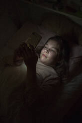 Girl using smart phone while lying in bedroom at night - JOSEF01554