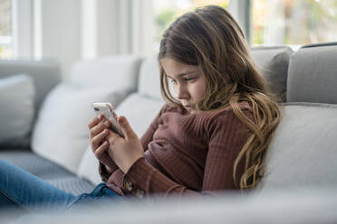 Girl using smart phone while sitting on sofa - JOSEF01556