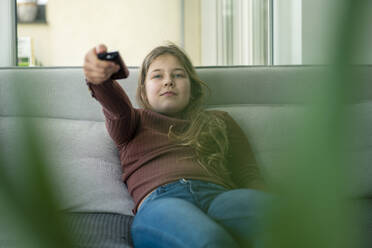 Girl using remote control while sitting on sofa - JOSEF01559