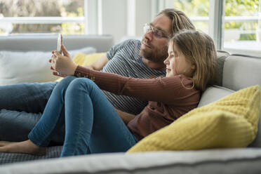 daughter taking selfie through phone with father on sofa - JOSEF01565