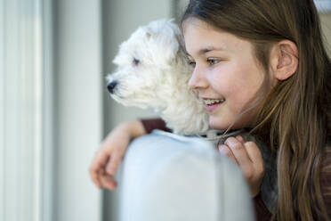 Nettes lächelndes Mädchen mit Hund, das im Wohnzimmer wegschaut - JOSEF01566