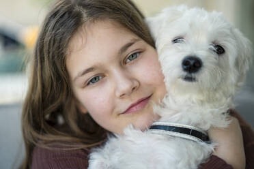 Cute smiling girl embracing dog in living room - JOSEF01568