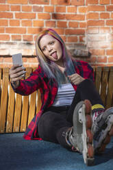 Young woman with dyed hair and roller skates taking a selfie and sticking out her tongue - VPIF02848