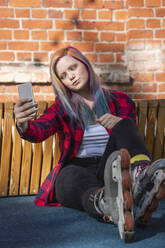 Young woman with dyed hair and roller skates taking a selfie with her smartphone, crosseyed - VPIF02849