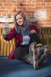 Young woman with dyed hair and roller skates taking a selfie with her smartphone - VPIF02850