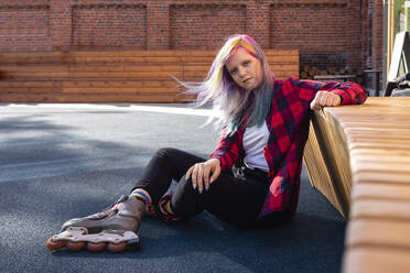 Young woman with dyed hair and roller skates sitting on ground - VPIF02852