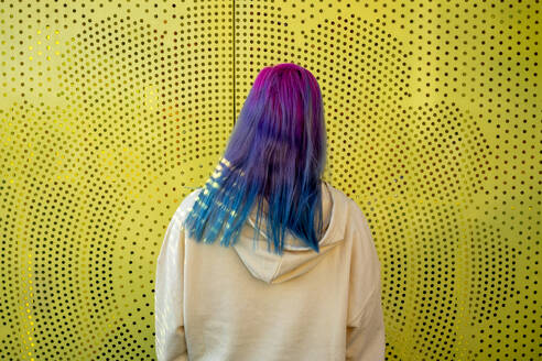 Rückansicht einer jungen Frau mit gefärbtem Haar vor einer gelben Wand - VPIF02856