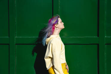 Portrait of young woman with dyed hair in front of green container - VPIF02863