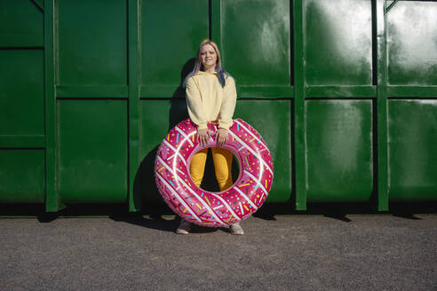 Junge Frau mit gefärbtem Haar und schwimmendem Reifen vor grünem Container - VPIF02864