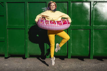 Young woman with dyed hair and floating tyre dancing in front of green container - VPIF02870