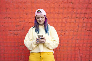 Porträt einer jungen Frau mit gefärbtem Haar, die ein Smartphone vor einer gelben Wand benutzt - VPIF02876