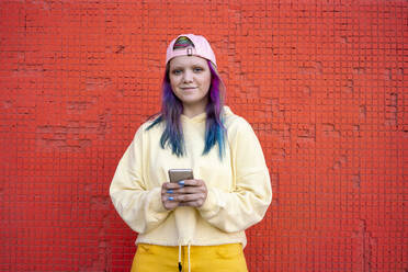 Portrait of young woman with dyed hair using smartphone in front of yellow wall - VPIF02877