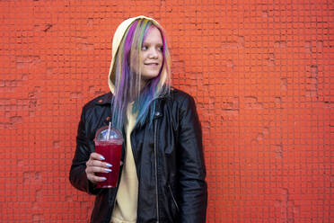 Porträt einer jungen Frau mit gefärbtem Haar und einem Getränk zum Mitnehmen vor einer roten Wand - VPIF02879