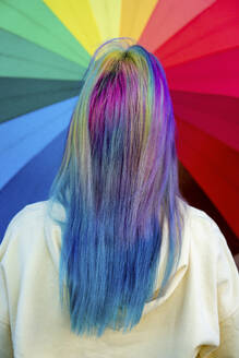 Rückansicht einer jungen Frau mit gefärbtem Haar vor einem Regenbogenschirm - VPIF02890