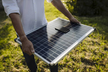 Mann hält Solarpanel mit Smartphone im Hof - GUSF04347