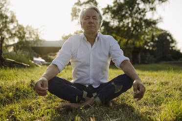 Man practicing yoga while sitting in lotus position at yard - GUSF04363