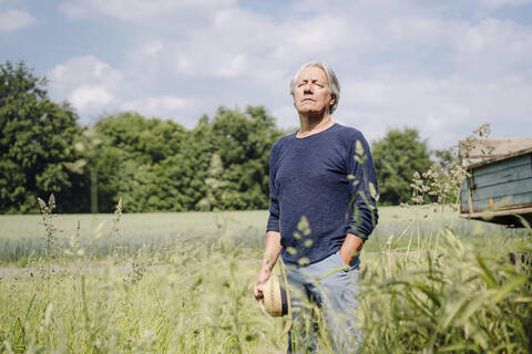 Wrinkled man holding hat standing in yard stock photo