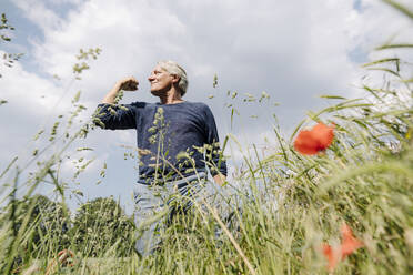 Selbstbewusster Mann, der seine Muskeln im Gras gegen den bewölkten Himmel anspannt - GUSF04408