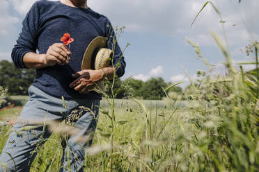 Mann mit Hut, der eine Blume hält, während er an einem sonnigen Tag auf einem Feld steht - GUSF04413