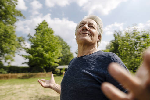 Confident wrinkled man with eyes closed enjoying in field during sunny day - GUSF04424