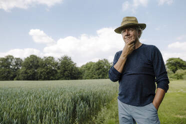 Nachdenklicher Mann, der mit der Hand am Kinn wegschaut, während er auf einem Feld gegen den Himmel steht - GUSF04425