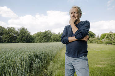 Runzliger Mann, der mit der Hand am Kinn wegschaut, während er auf einem Feld gegen den Himmel steht - GUSF04426