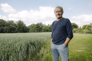 Lächelnder Mann mit Händen in den Taschen auf einem Feld - GUSF04427