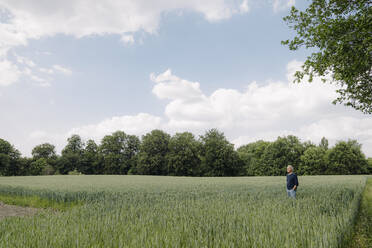 Mann mit Händen in den Taschen steht in einem landwirtschaftlichen Feld - GUSF04429