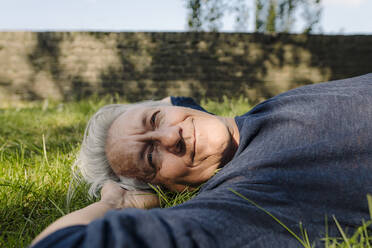 Confident smiling man lying in field - GUSF04434