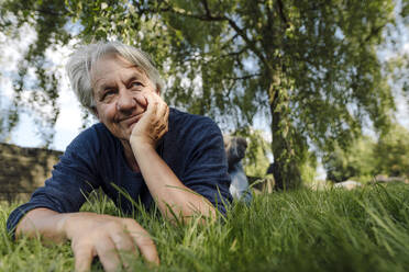 Confident smiling man lying on front in field - GUSF04435